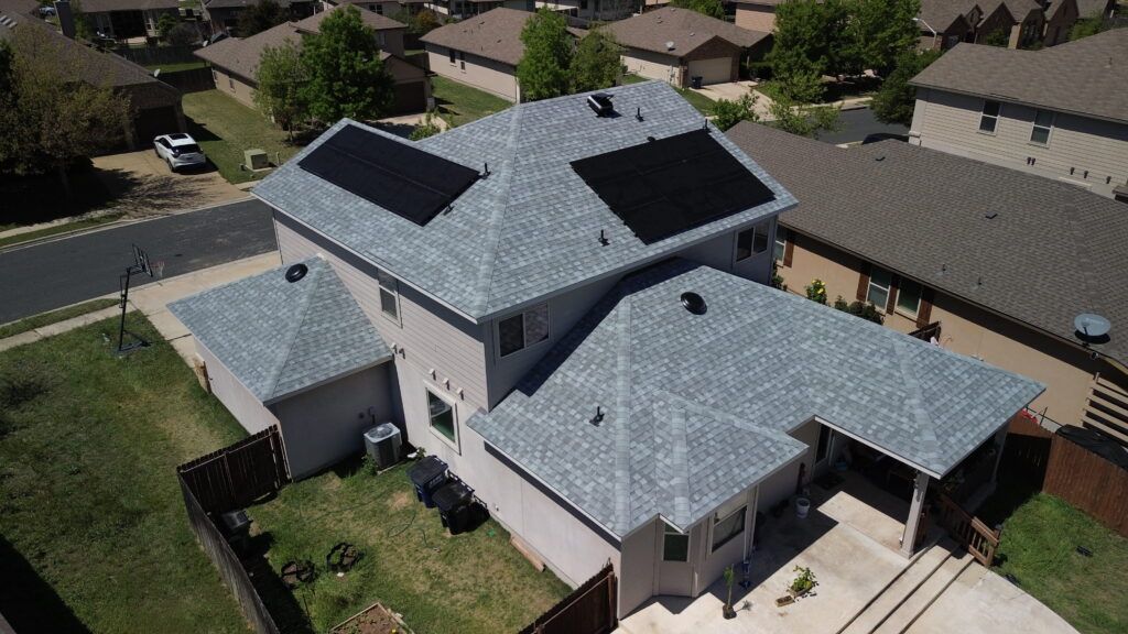 Aerial view of a two-story house with gray roof shingles and solar panels. A neighborhood surrounds the home.