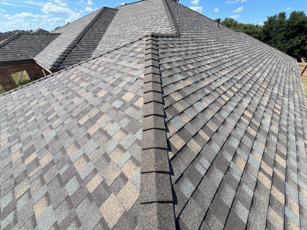 Close-up view of a multi-colored asphalt shingle roof on a house, with a blue sky background.