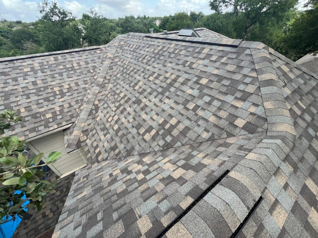 Close-up of a multi-colored shingle roof on a house with trees in the background.