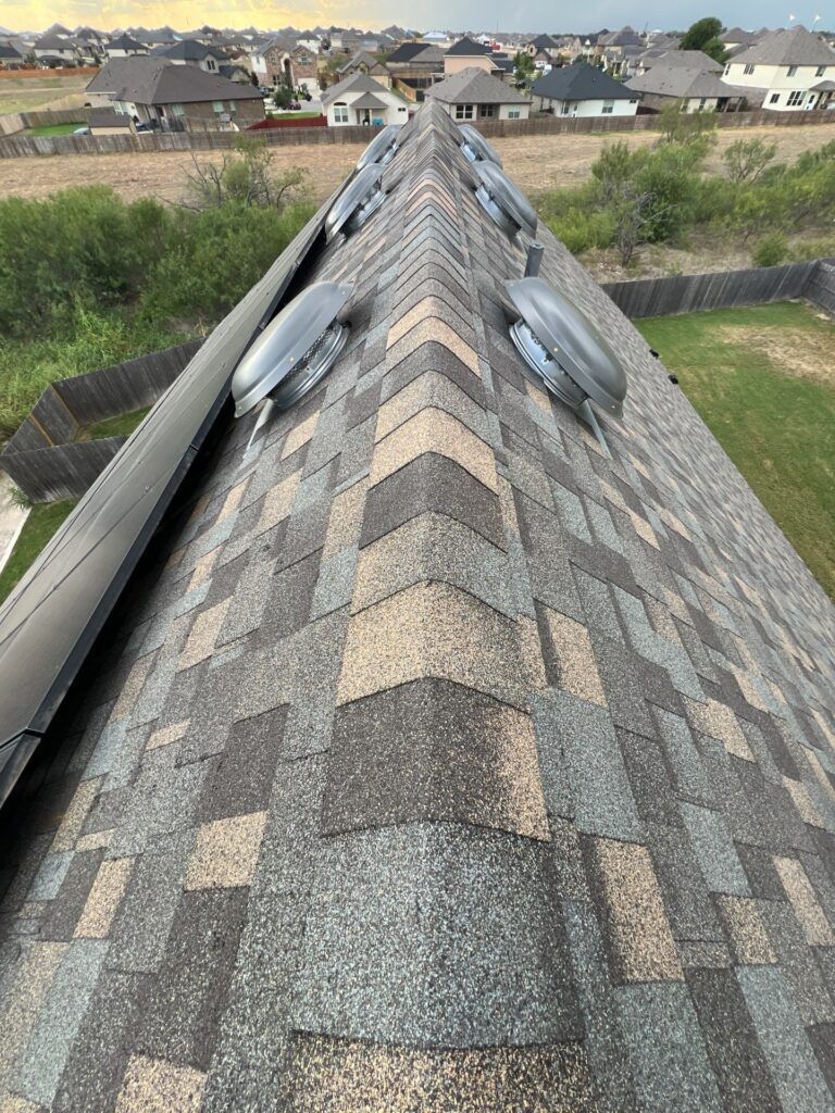 Close-up of a house roof with various colored shingles and several exhaust vents.