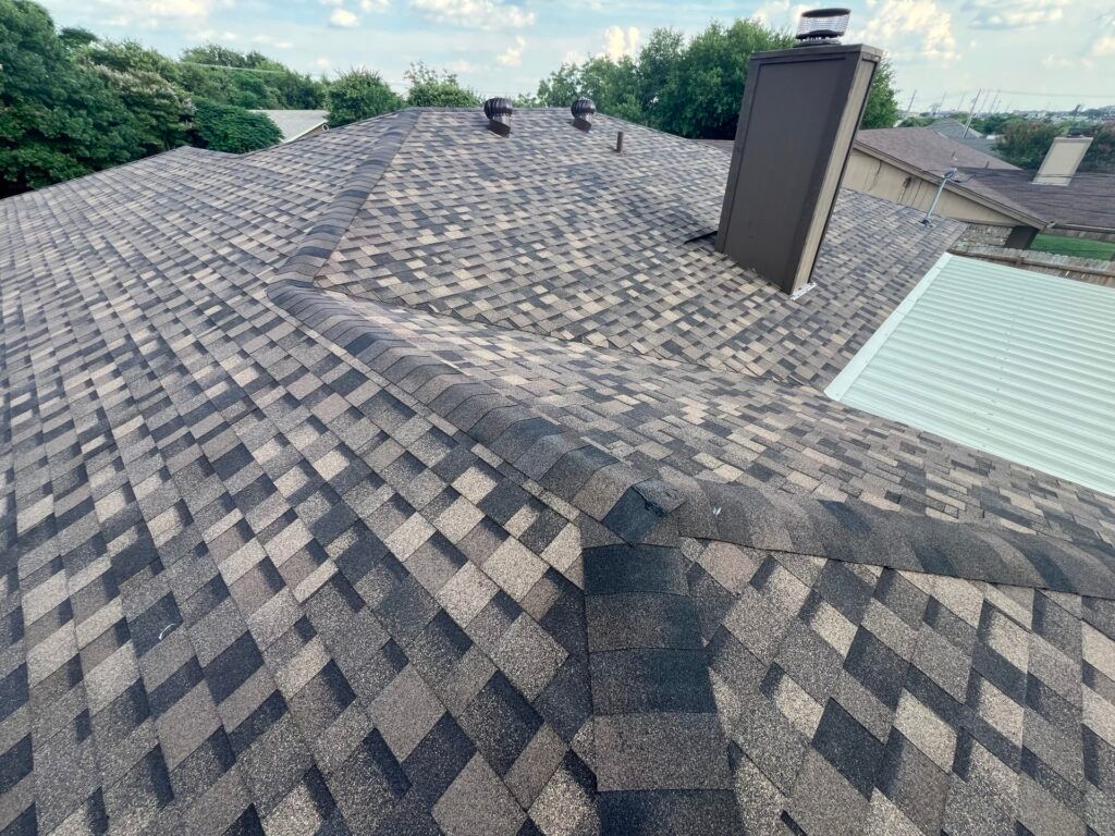 Close-up view of a multi-colored asphalt shingle roof with a chimney and vents on a house.