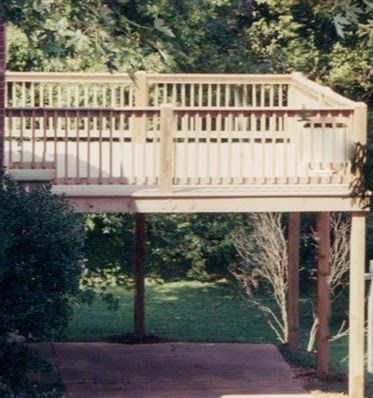 A wooden deck with a white railing is surrounded by trees