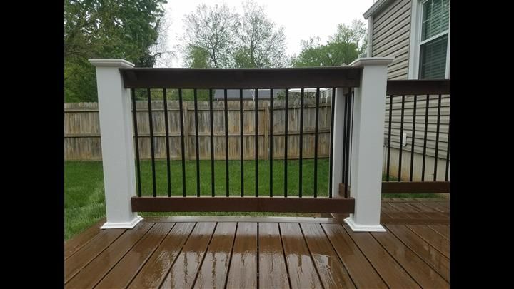 A wooden deck with a white railing and a fence in the background.