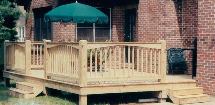 A wooden deck with a green umbrella in front of a brick house