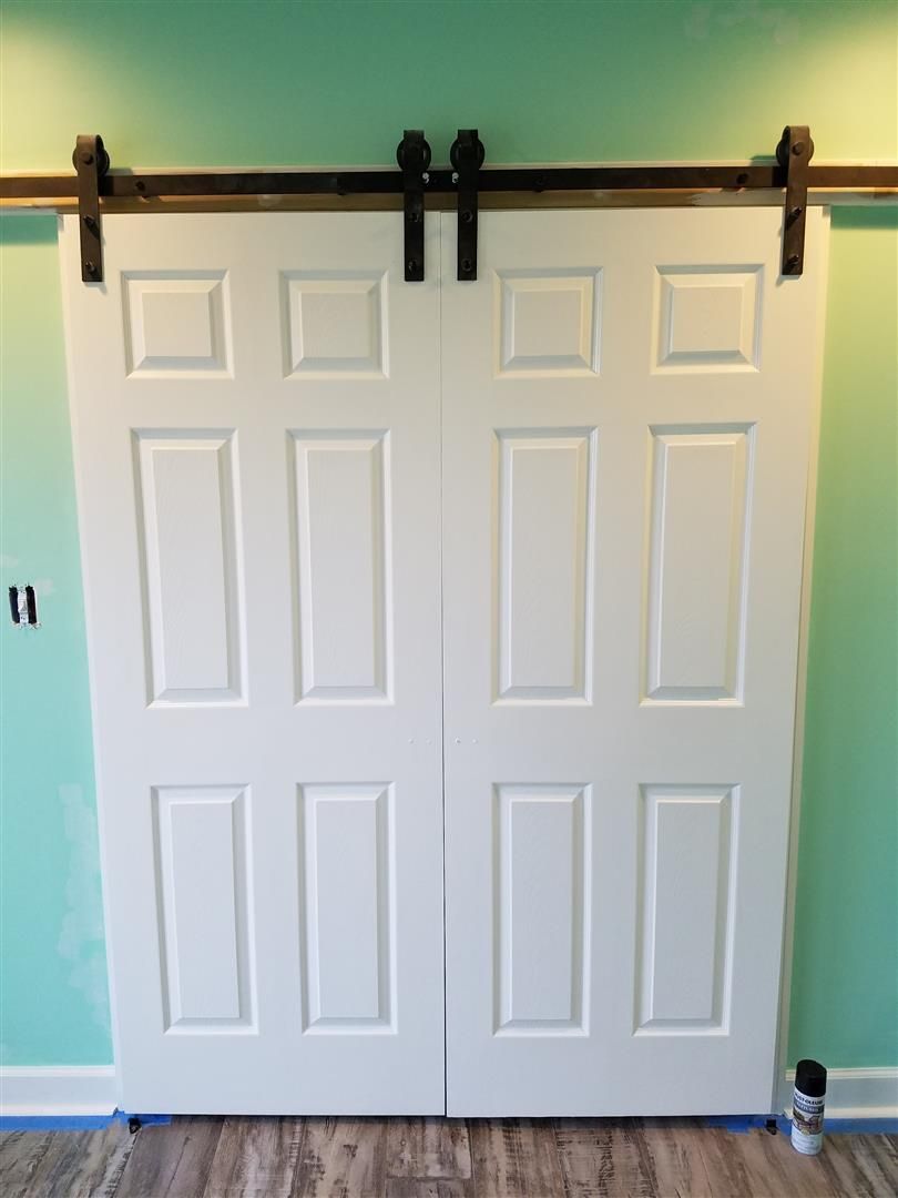 A pair of white sliding barn doors are hanging on a green wall.
