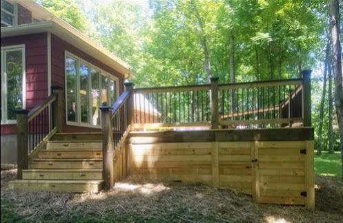 A wooden deck with stairs leading up to it is in front of a house surrounded by trees.