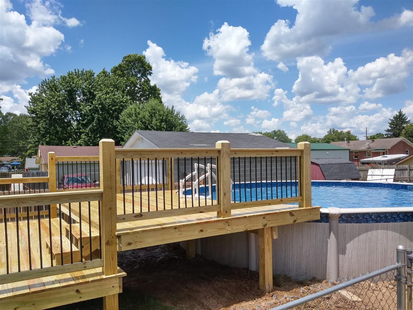 A wooden deck overlooking a swimming pool with a house in the background.