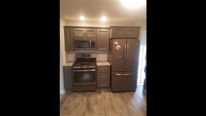 A kitchen with a stove , refrigerator , microwave and cabinets.