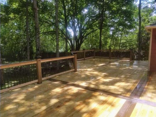 A wooden deck with a fence and trees in the background.
