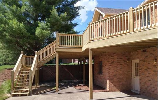 A wooden deck with stairs leading up to it is in front of a brick house.