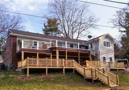 A large house with a wooden deck and stairs in front of it.