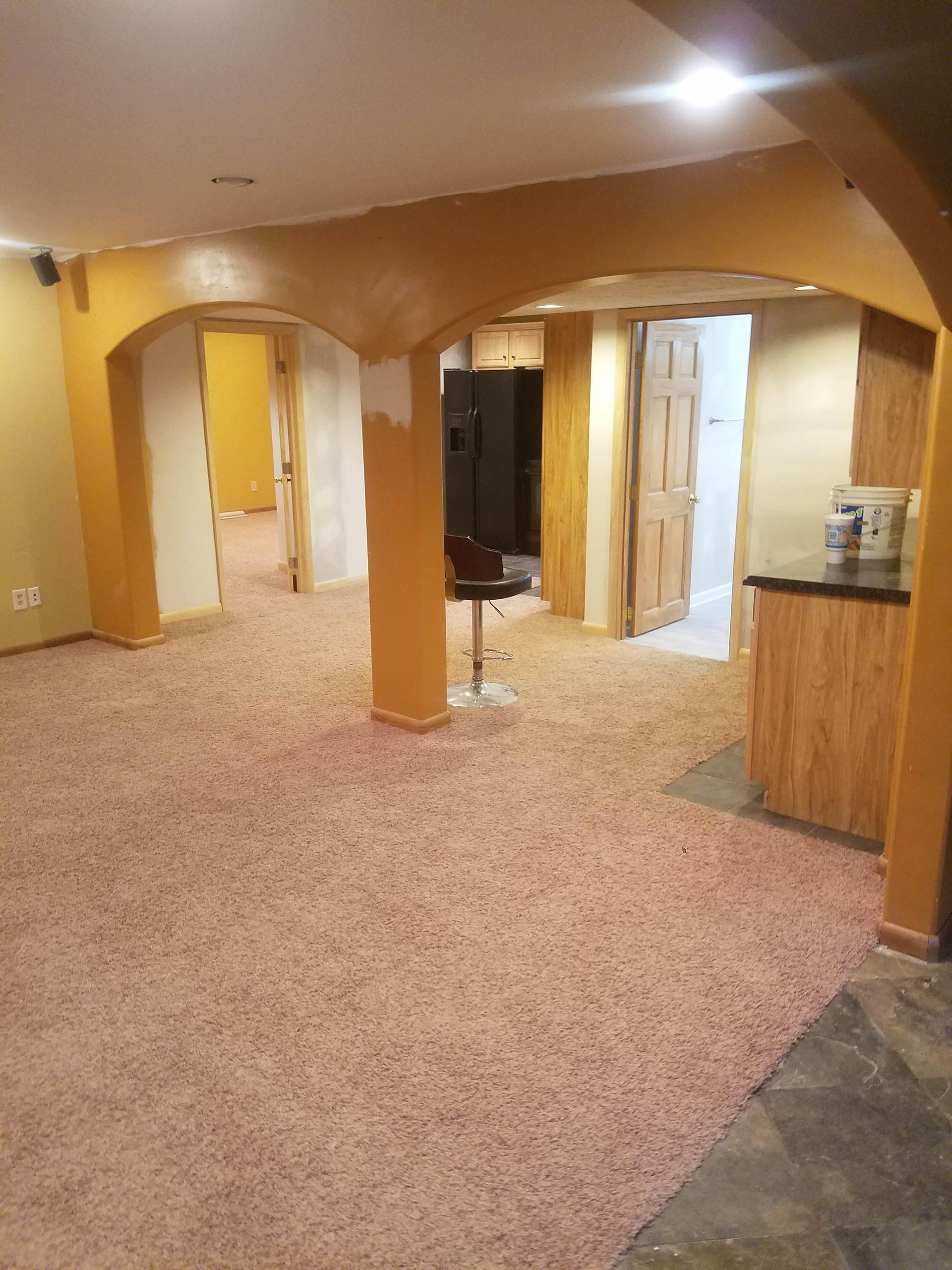 An empty basement with a carpeted floor and a bar stool.
