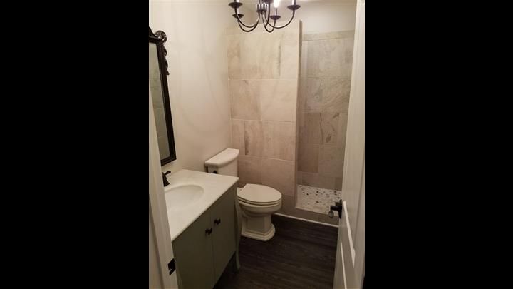 A bathroom with a toilet , sink , mirror and walk in shower.