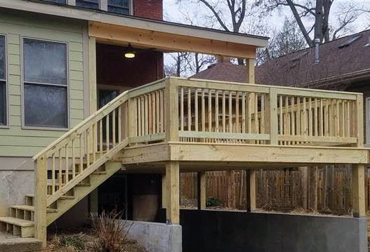A wooden deck with stairs leading up to it is in front of a house.