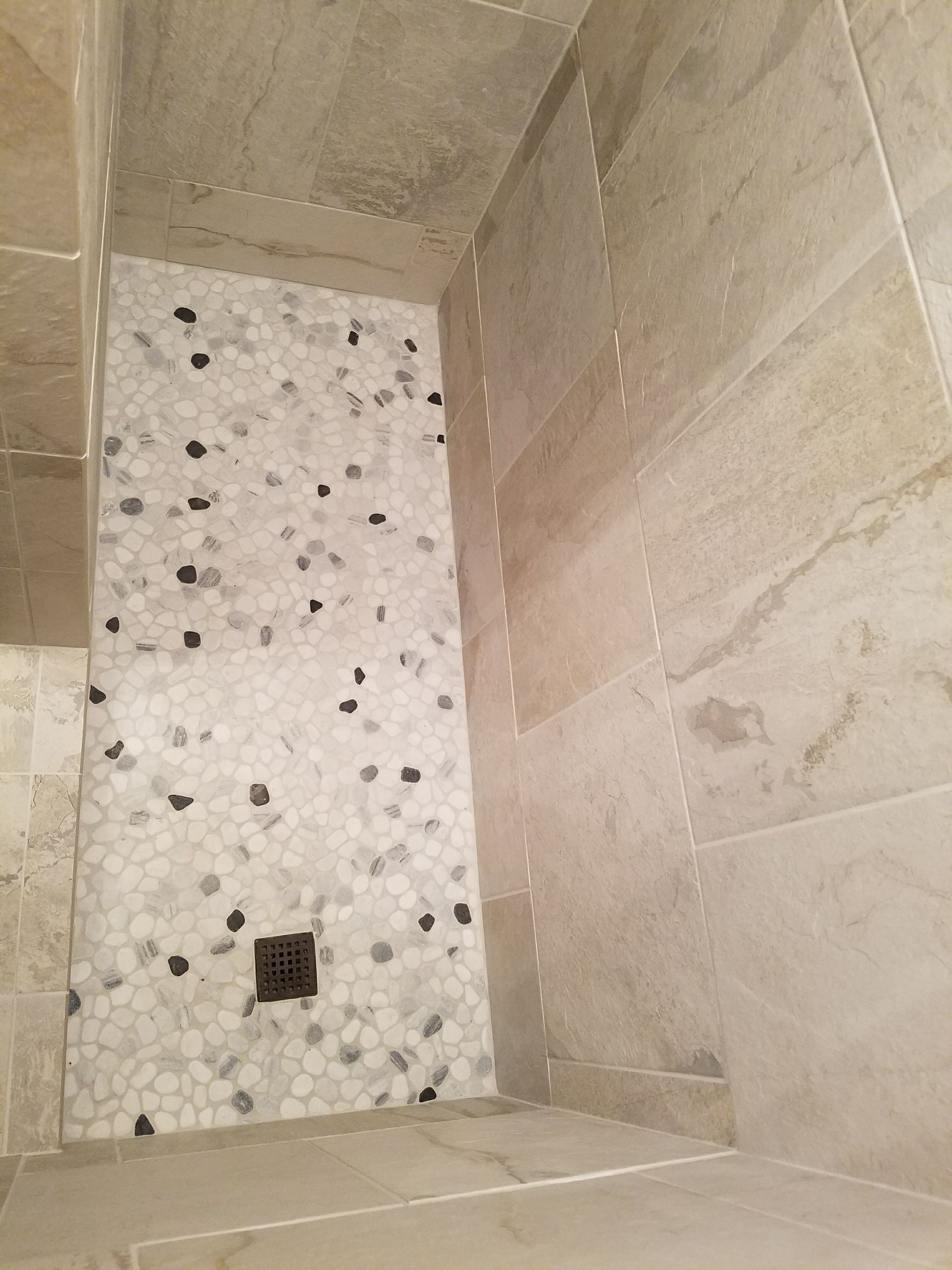 A shower stall with a tiled floor and a black drain.