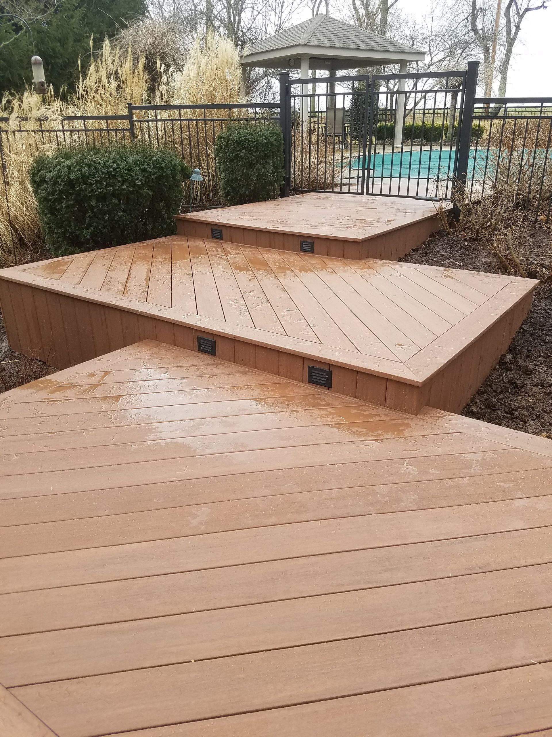 A wooden deck with stairs leading up to it and a gazebo in the background.