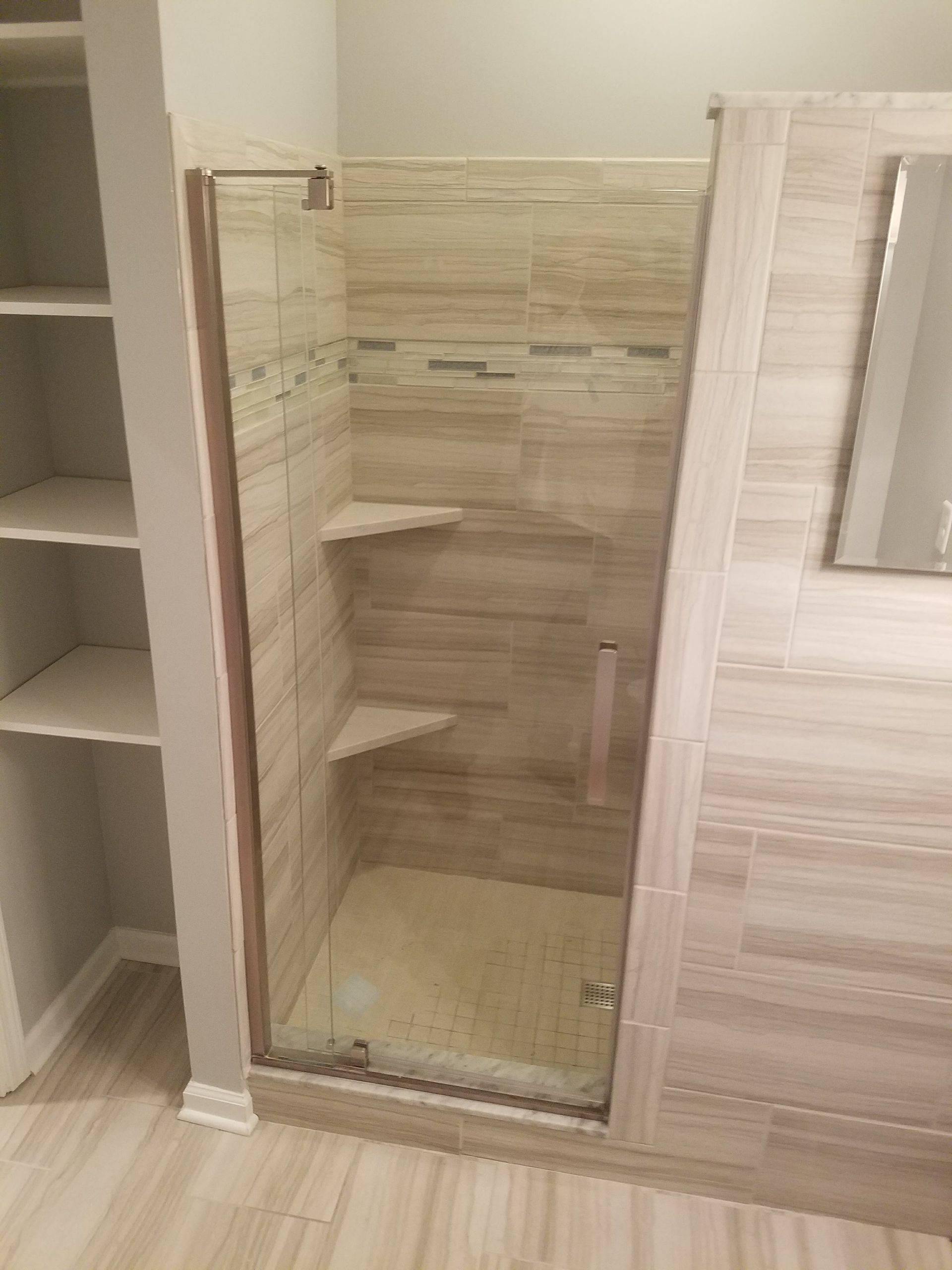 A bathroom with a walk in shower with a glass door and shelves.