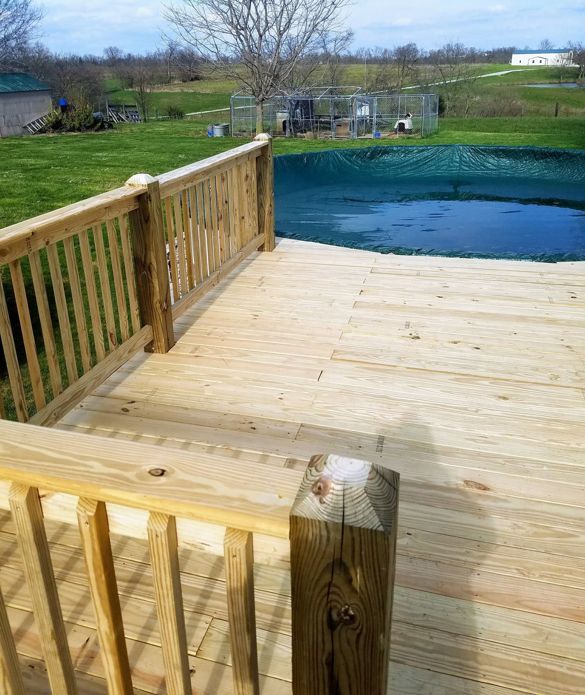 A wooden deck with a railing and a pond in the background.
