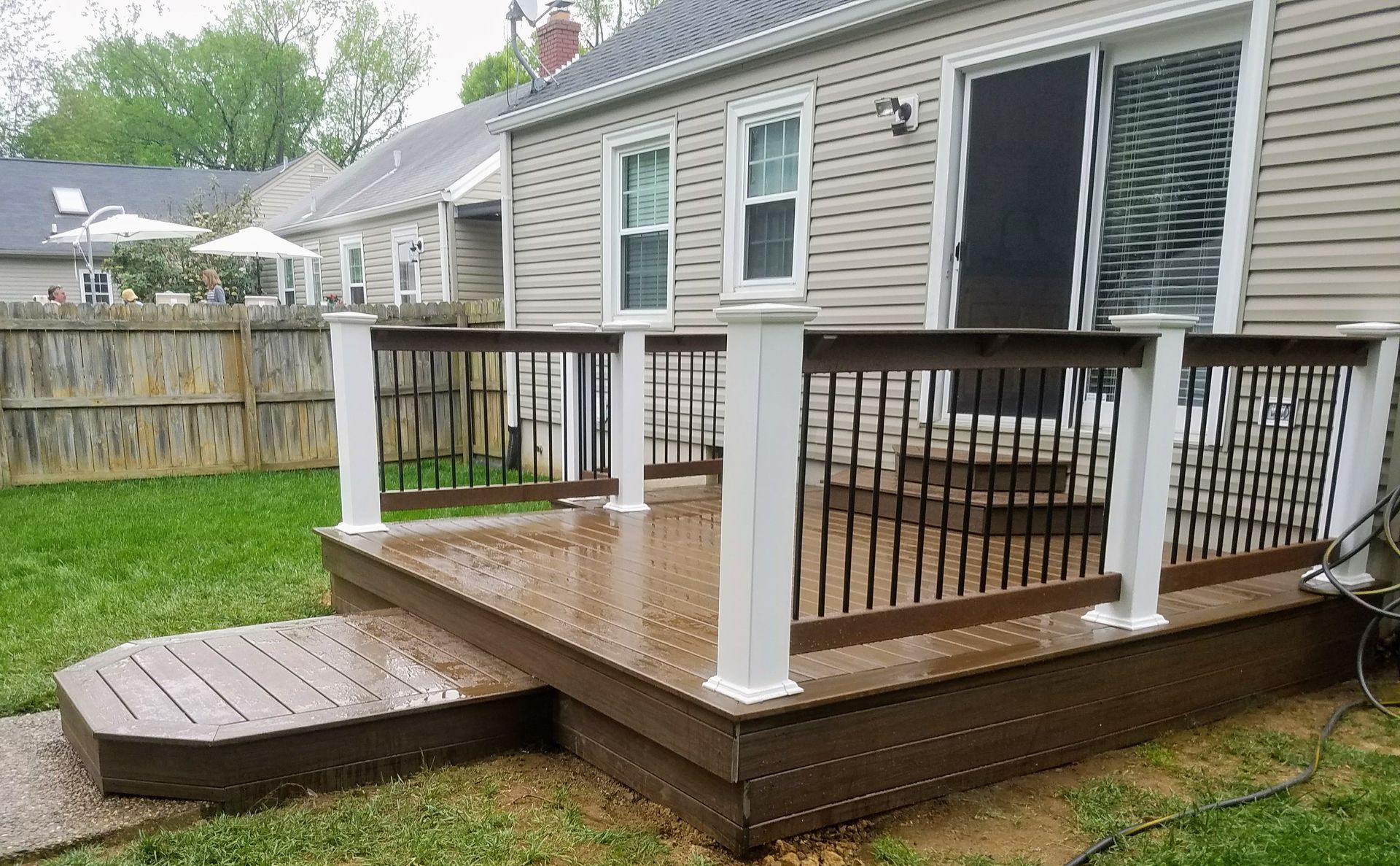 A wooden deck with a white railing is in the backyard of a house.