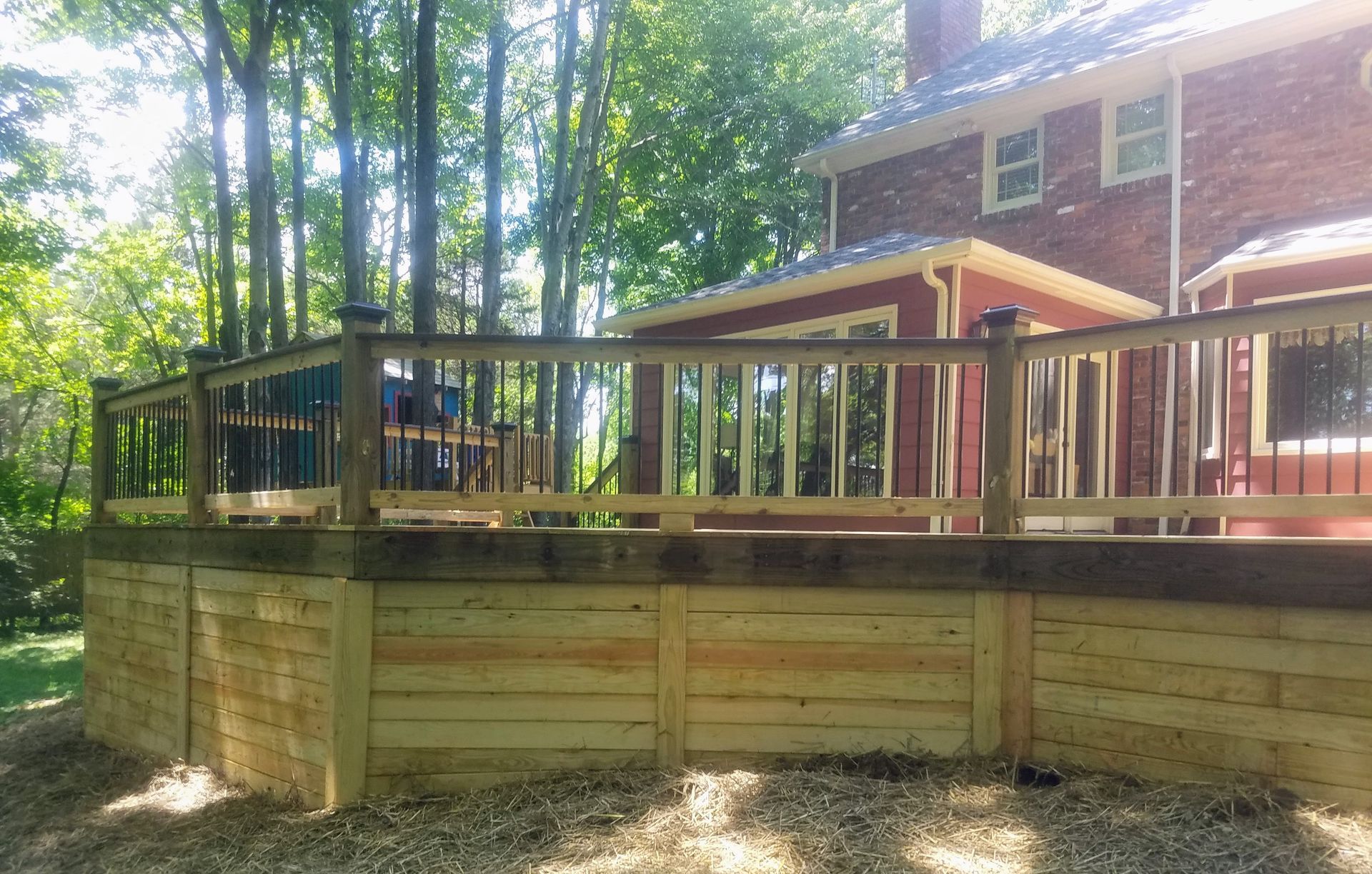 A wooden deck with a railing in front of a brick house.