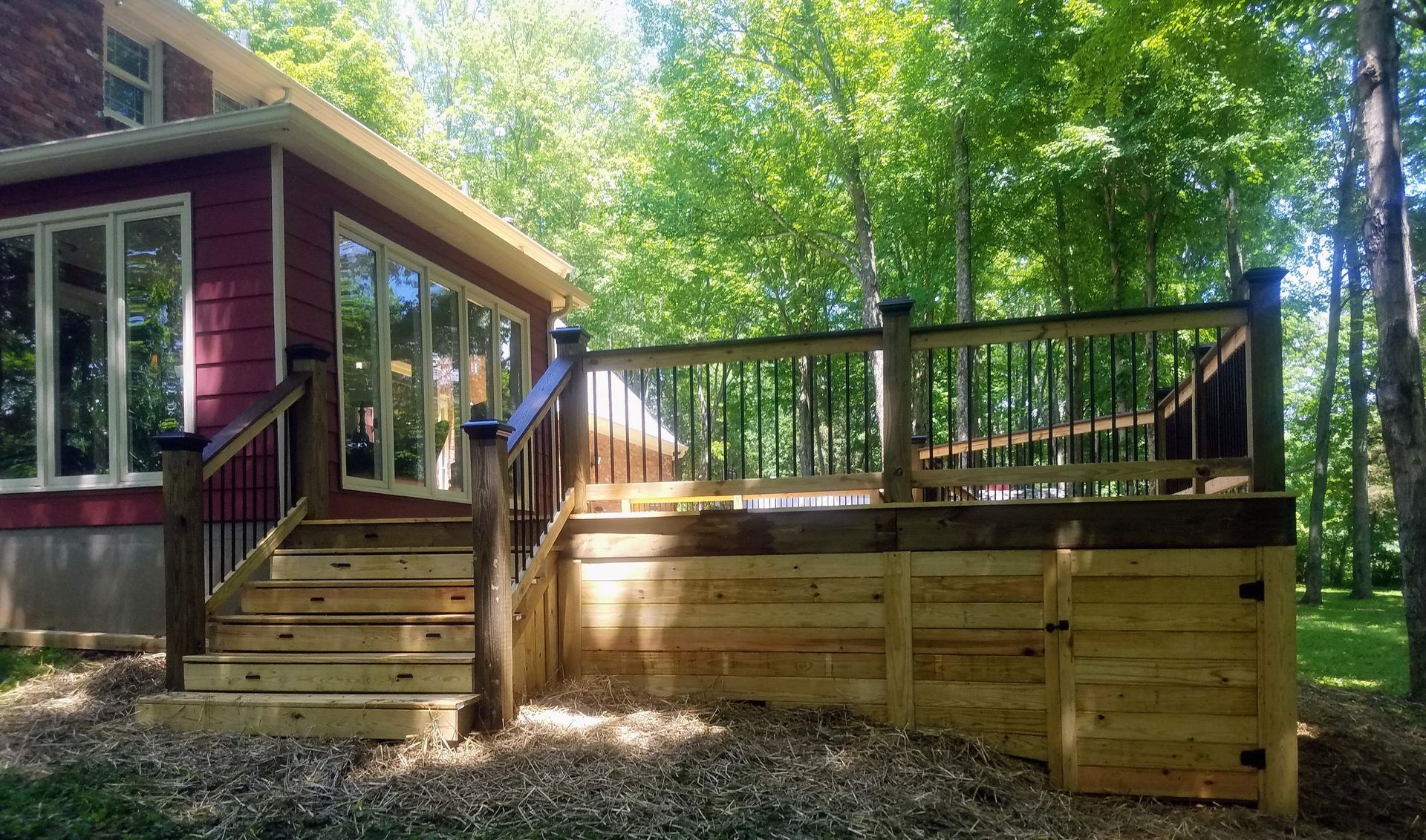 A wooden deck with stairs and a fence in front of a house surrounded by trees.