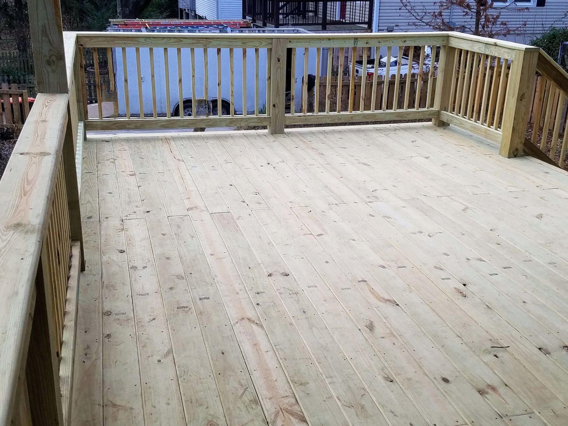A wooden deck with a railing and a white house in the background