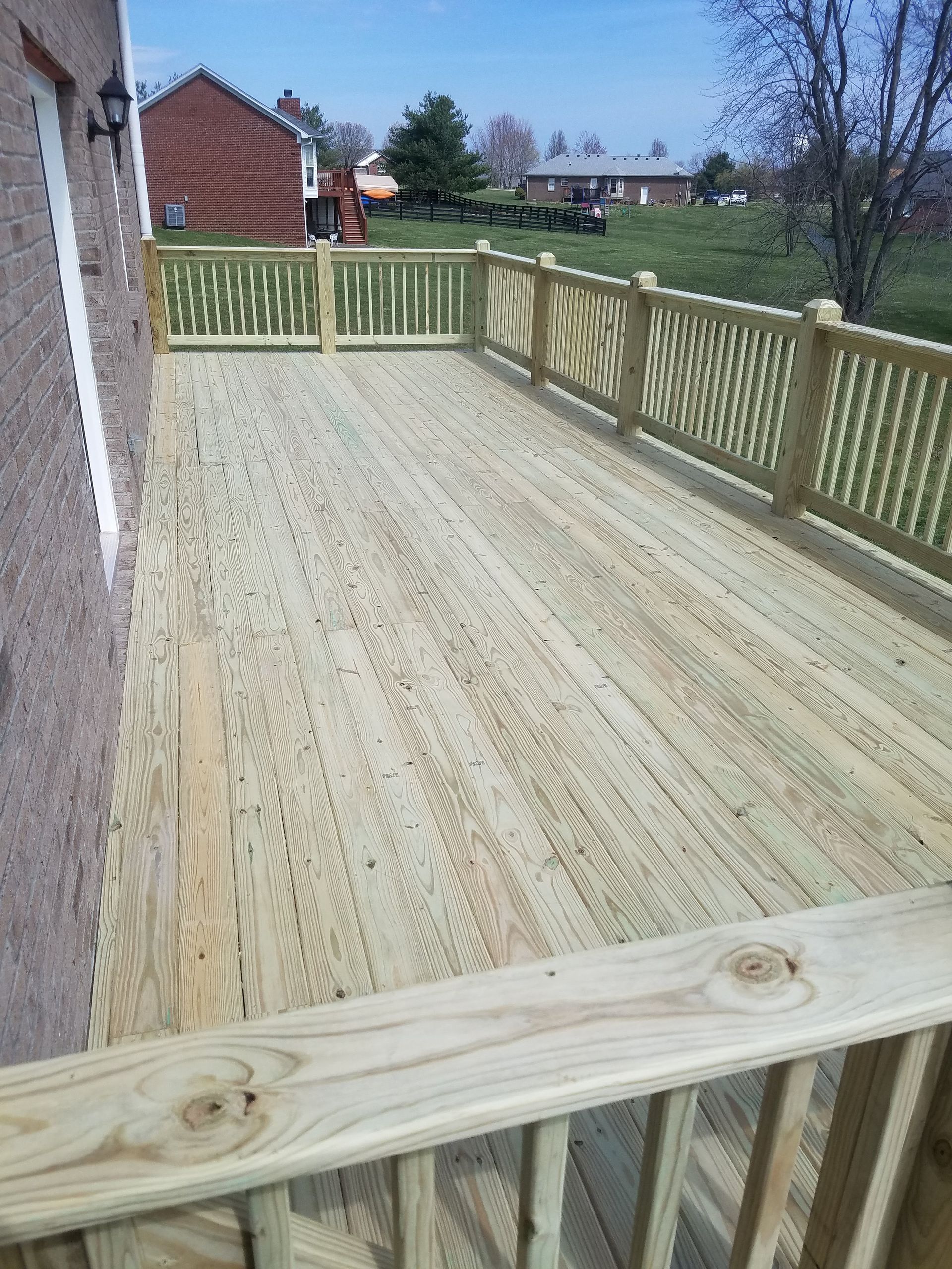 A large wooden deck with a fence around it and a house in the background.