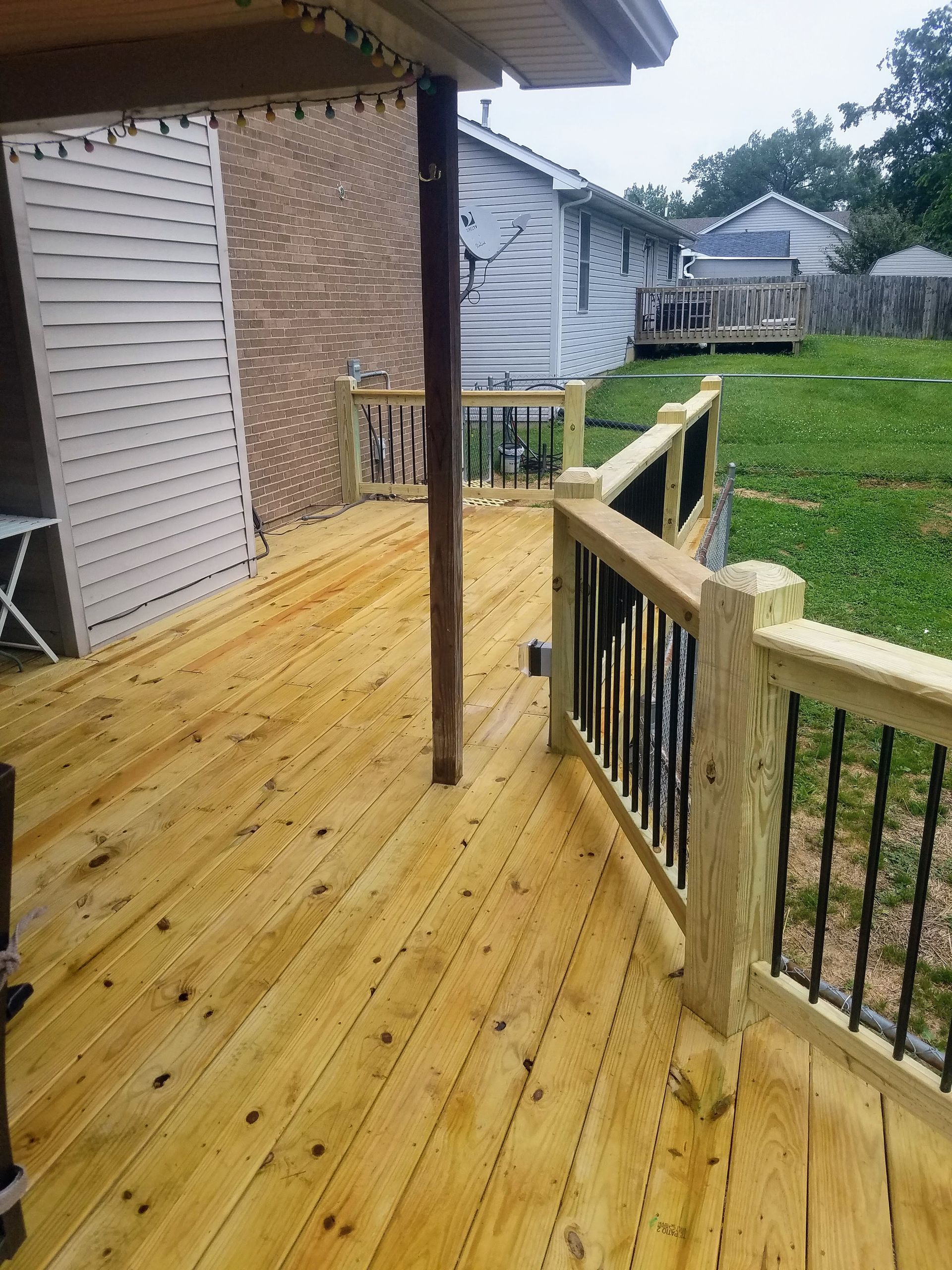 A wooden deck with a metal railing and a house in the background.