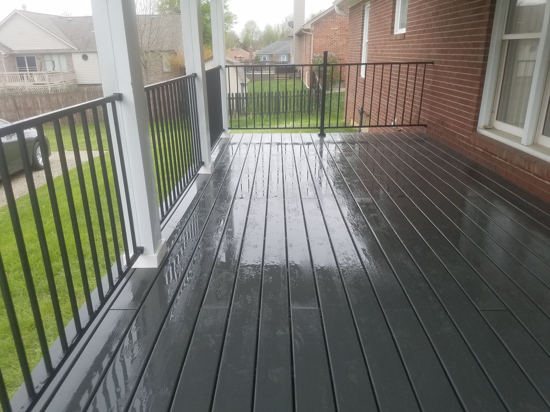 A black deck with a metal railing and a brick house in the background.