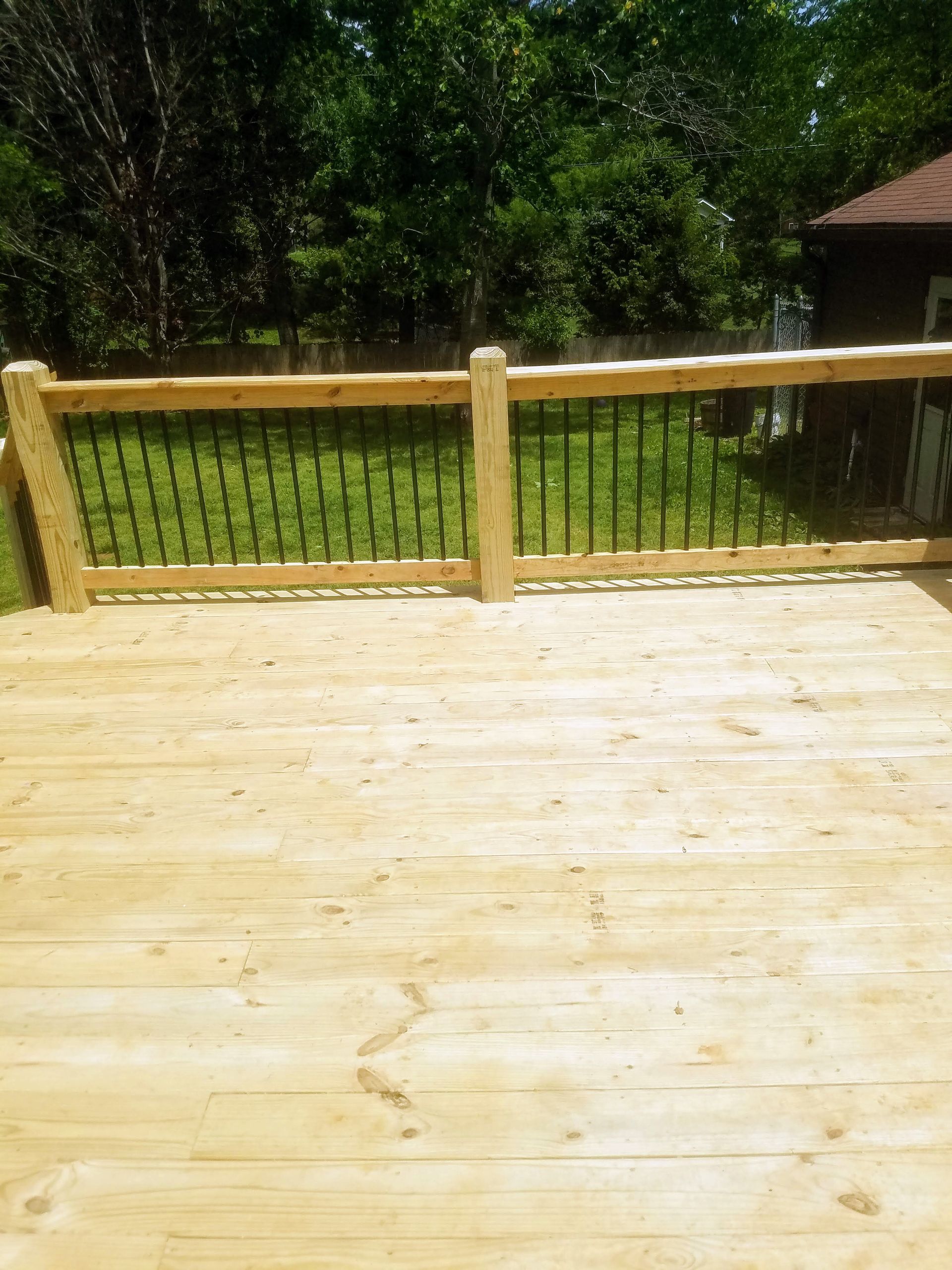 A wooden deck with a metal railing and trees in the background.