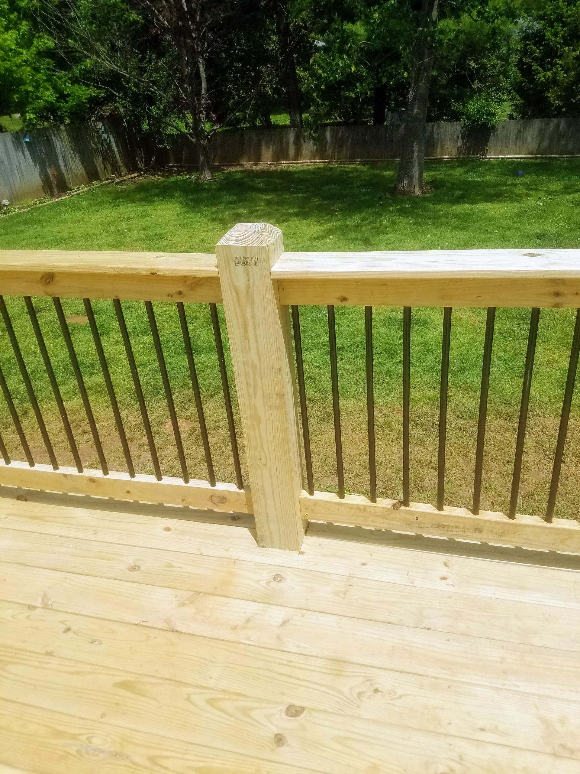 A wooden deck with a metal railing and a fence in the background.