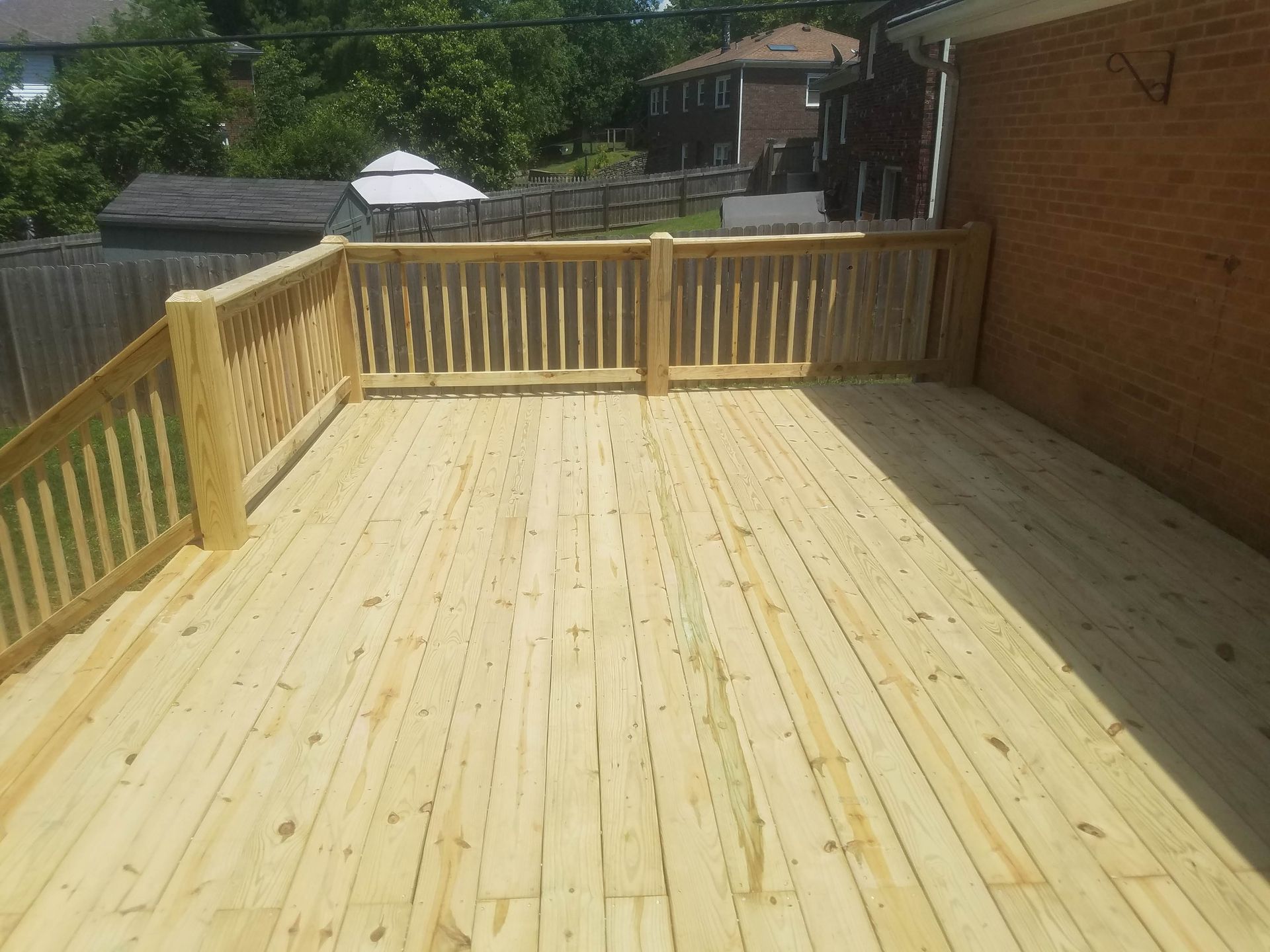 A large wooden deck with a wooden railing is sitting in front of a brick house.