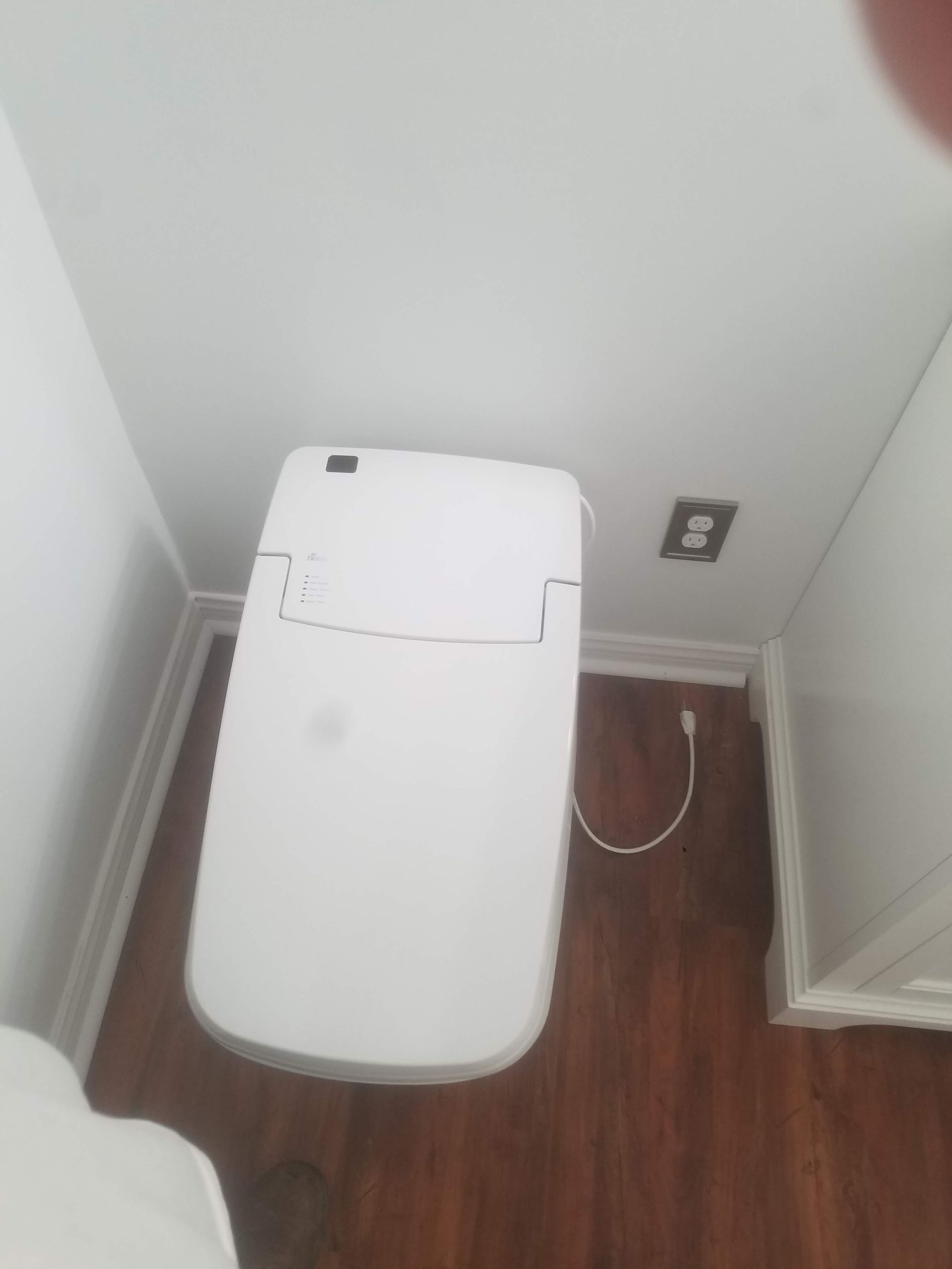 A white toilet is sitting in a corner of a bathroom next to a wooden floor.
