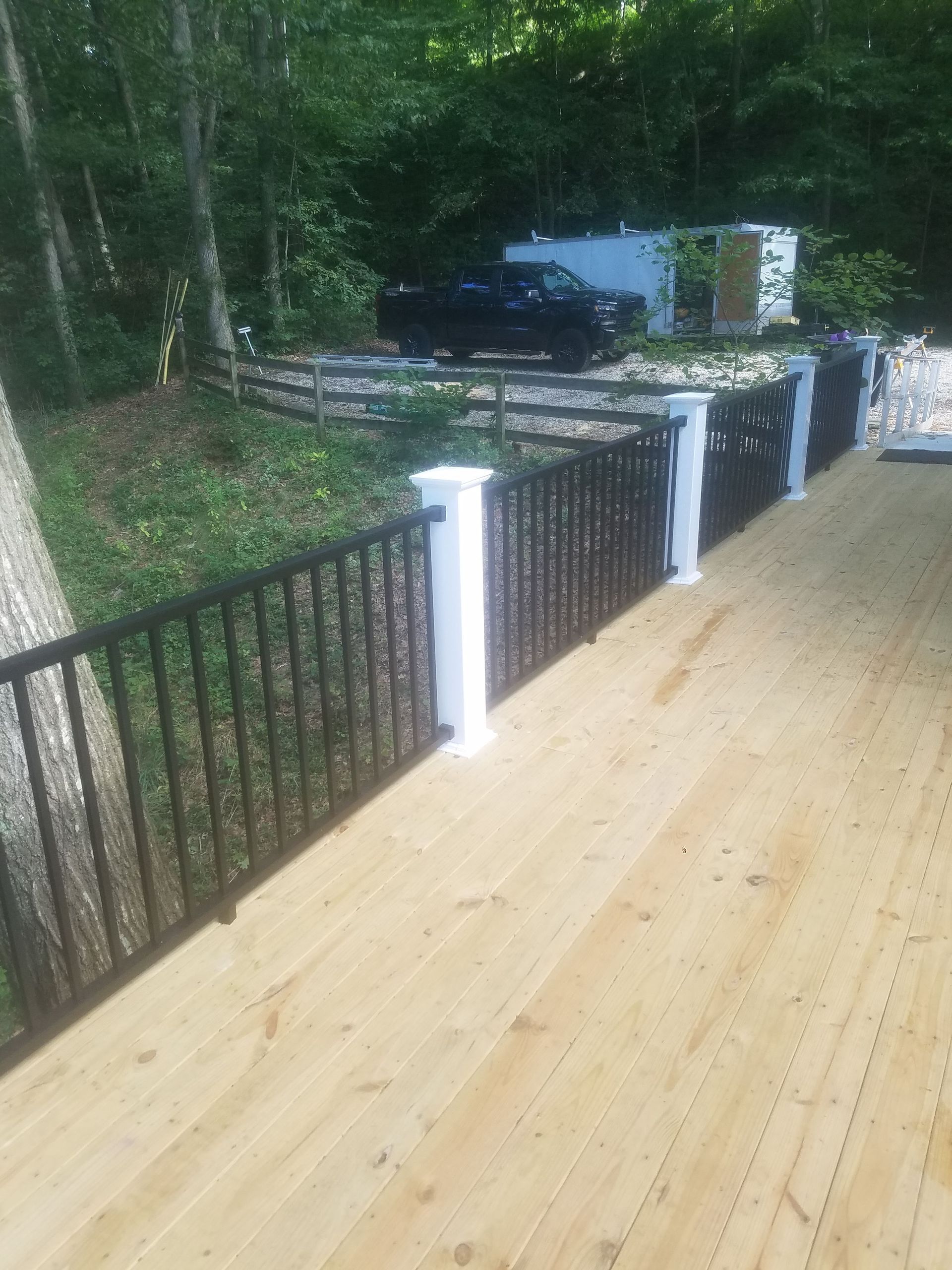 A wooden deck with a black railing and a car parked in the background.