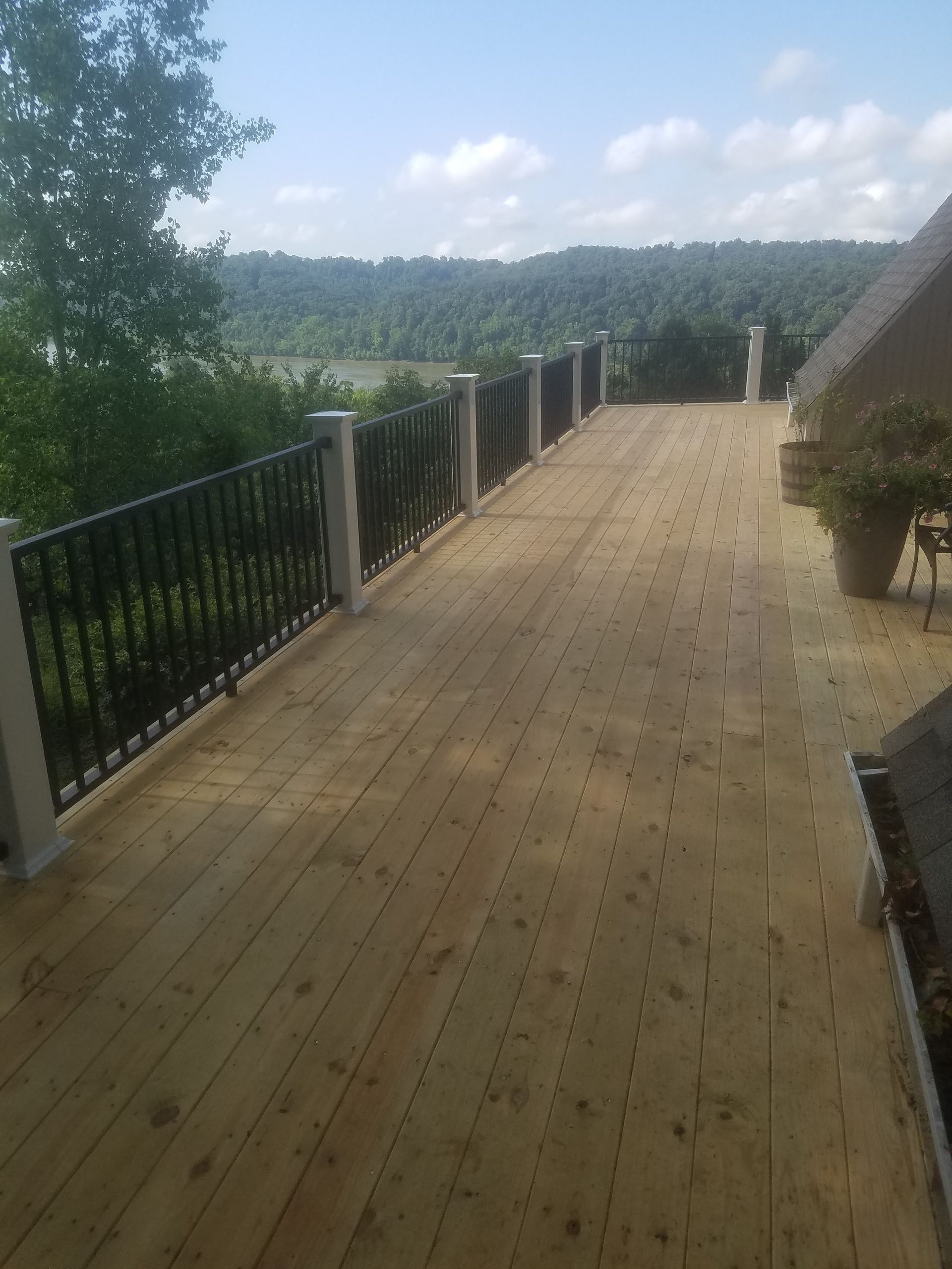 A wooden deck with a black railing and a view of a river.