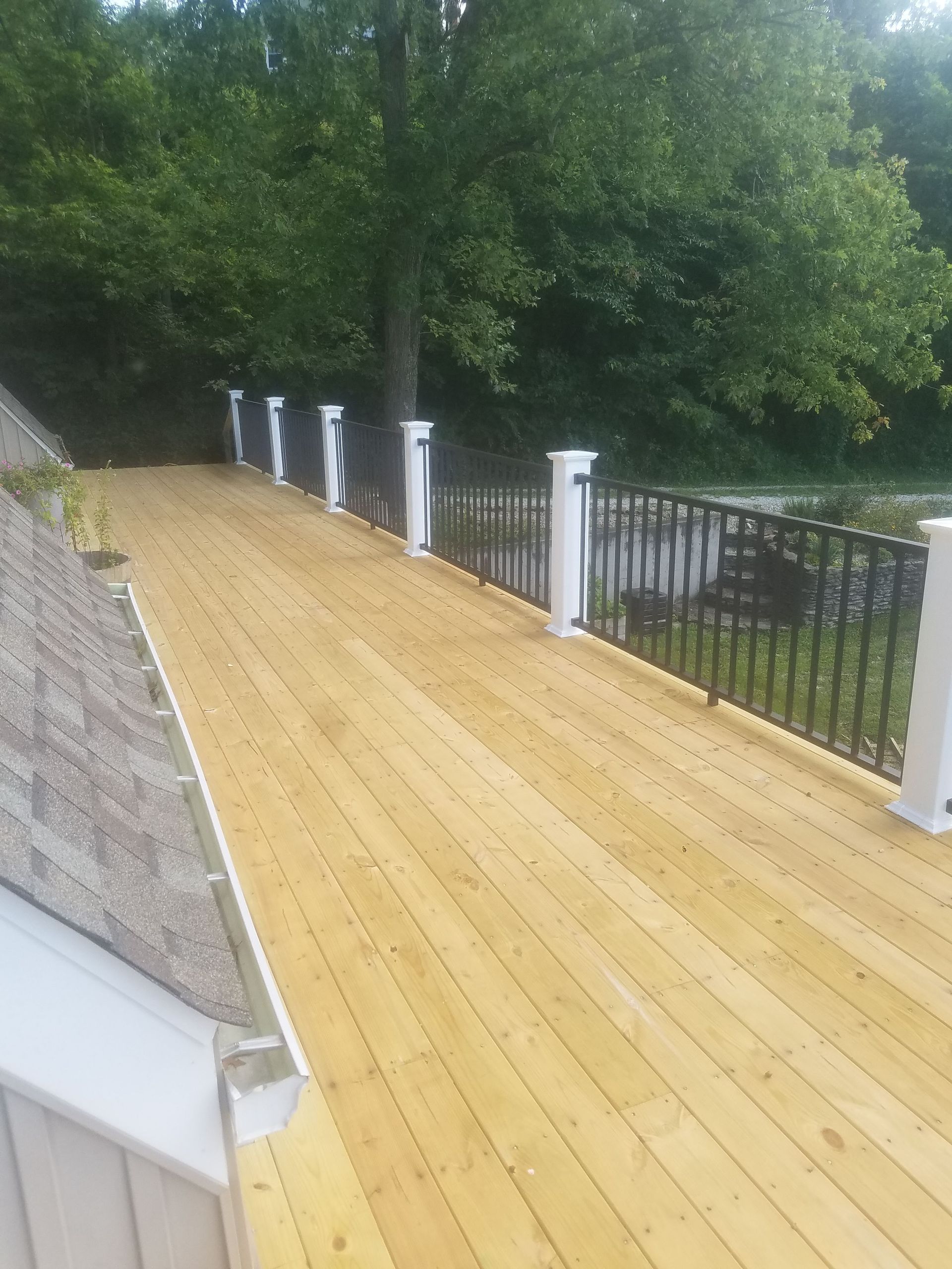 A wooden deck with a white railing and trees in the background.
