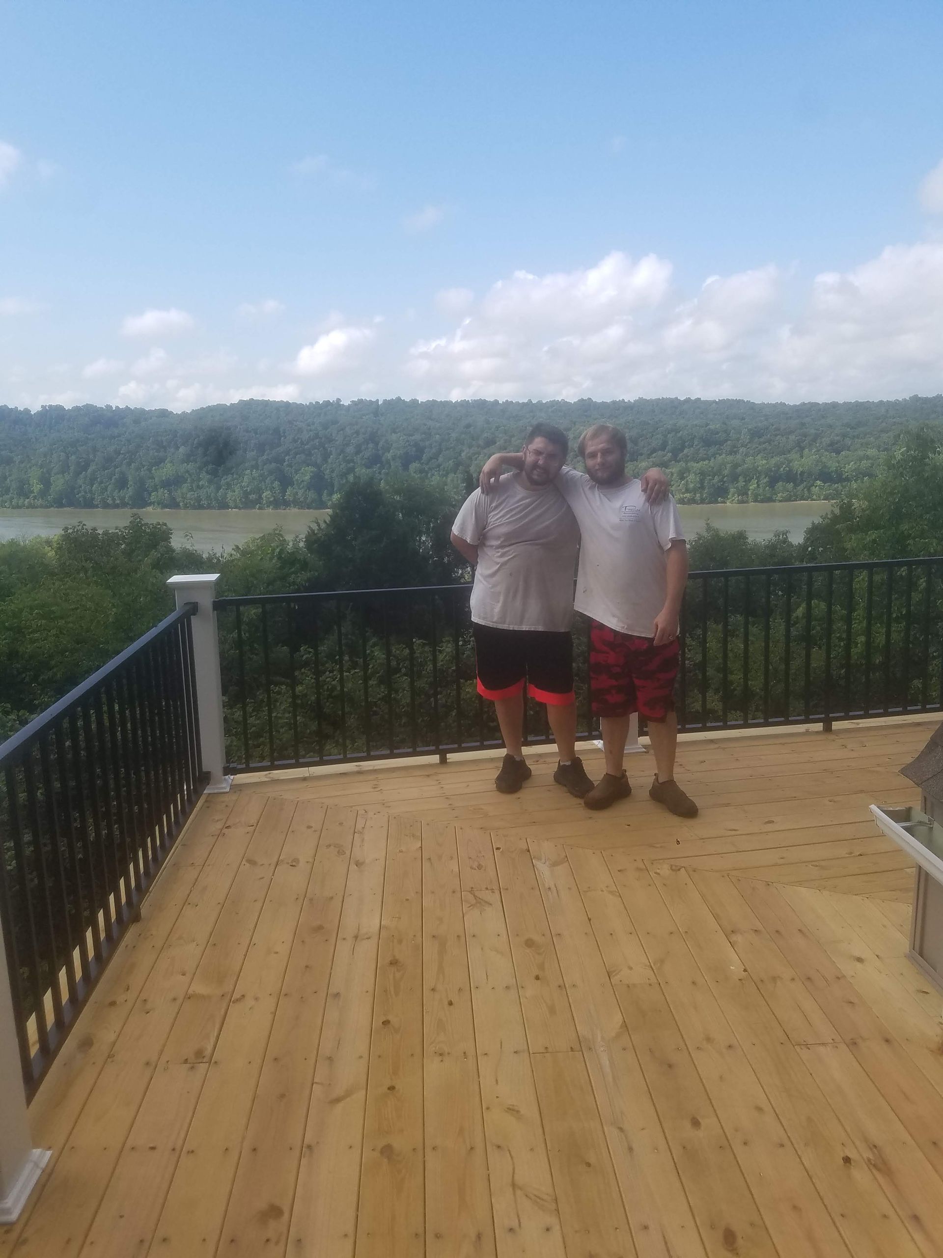 Two men are standing on a wooden deck overlooking a river.