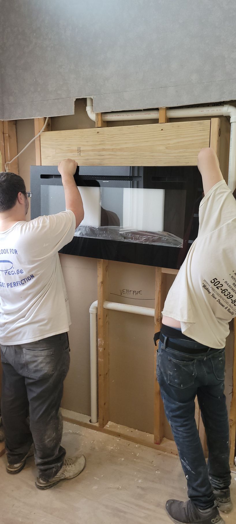 Two men are installing a fireplace in a room.
