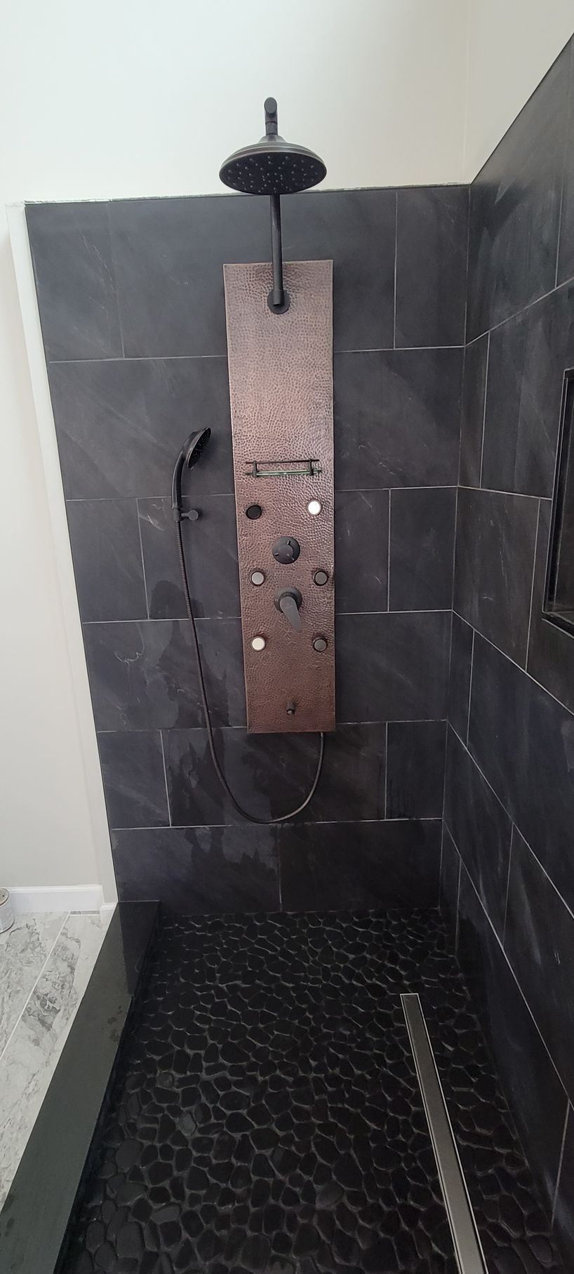 A shower with a black tile floor and a copper shower head.