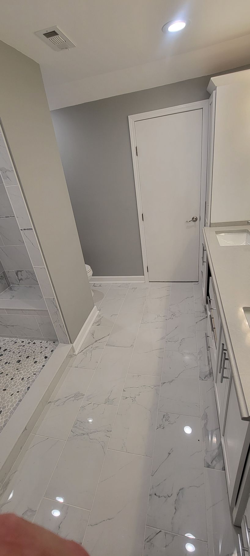 A bathroom with a marble floor and white cabinets.