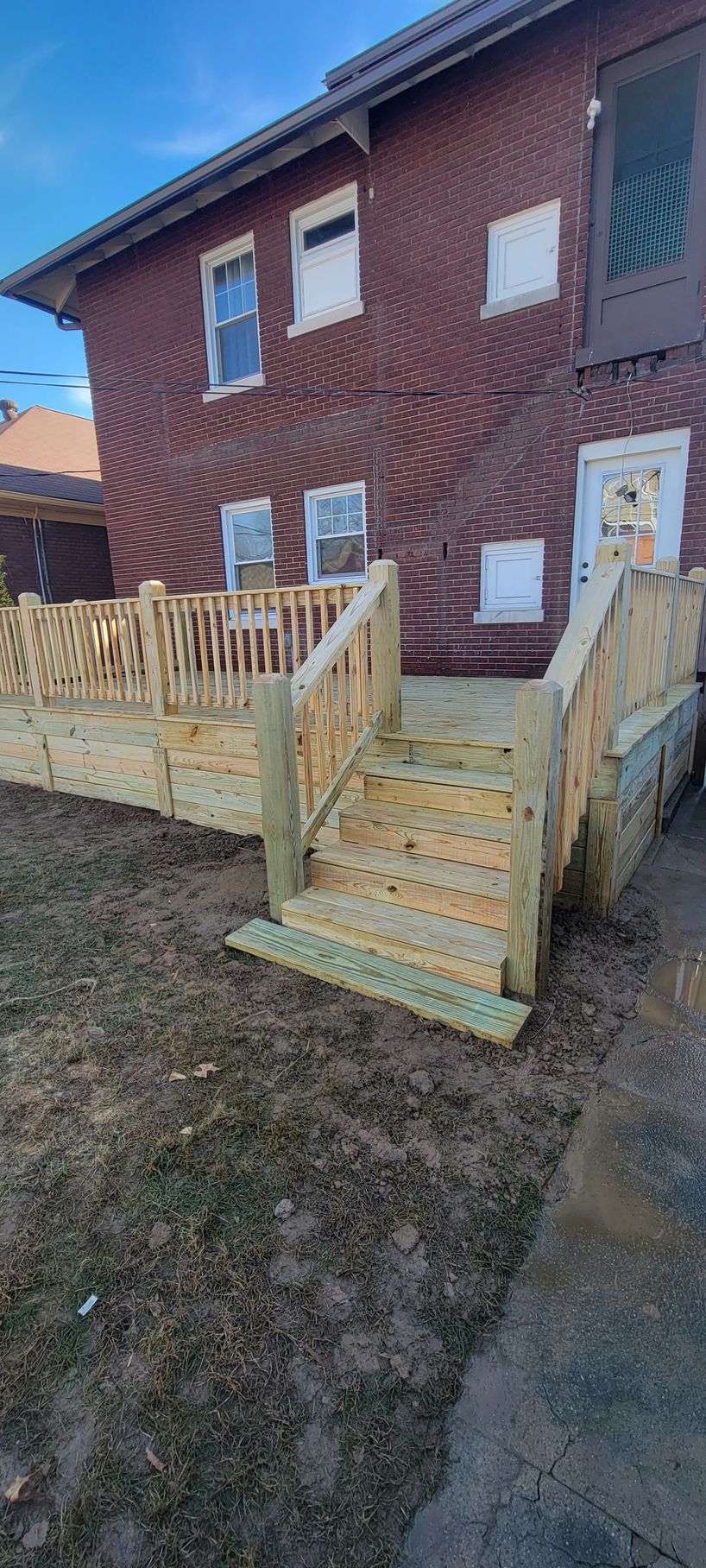 A wooden deck with stairs is in front of a brick building.