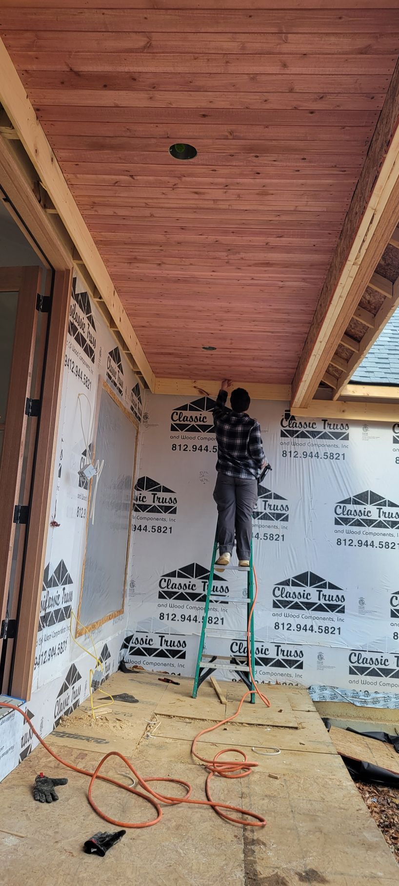A man is standing on a ladder in a room with a wooden ceiling.