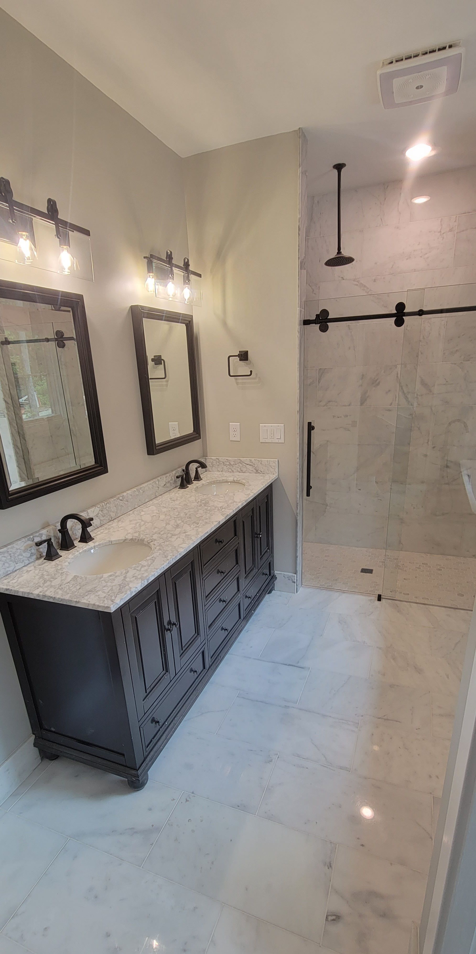 A bathroom with two sinks , two mirrors and a walk in shower.