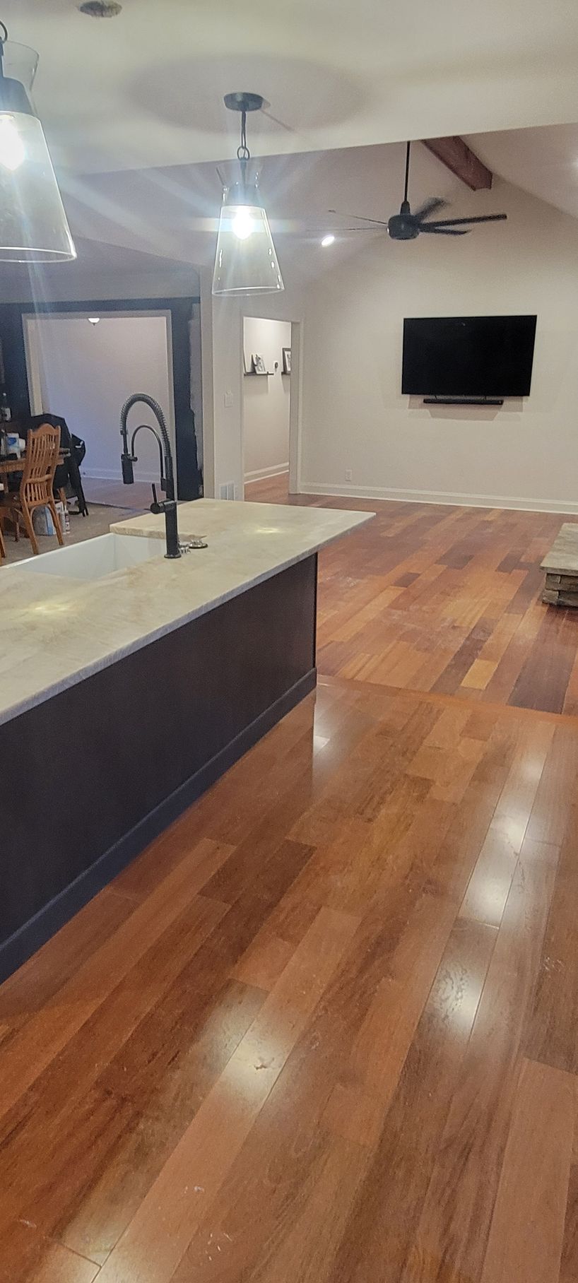 A kitchen with hardwood floors , a sink , and a flat screen tv.