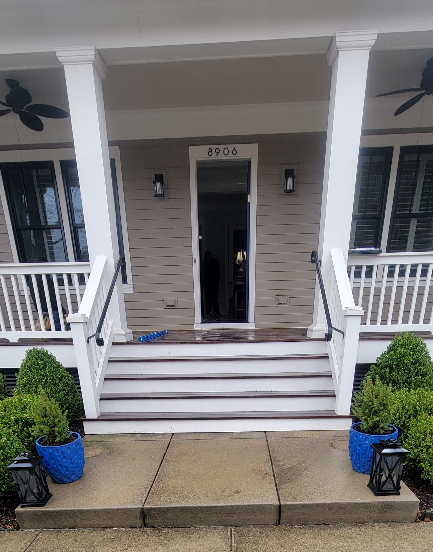 The front porch of a house with blue potted plants and a ceiling fan.