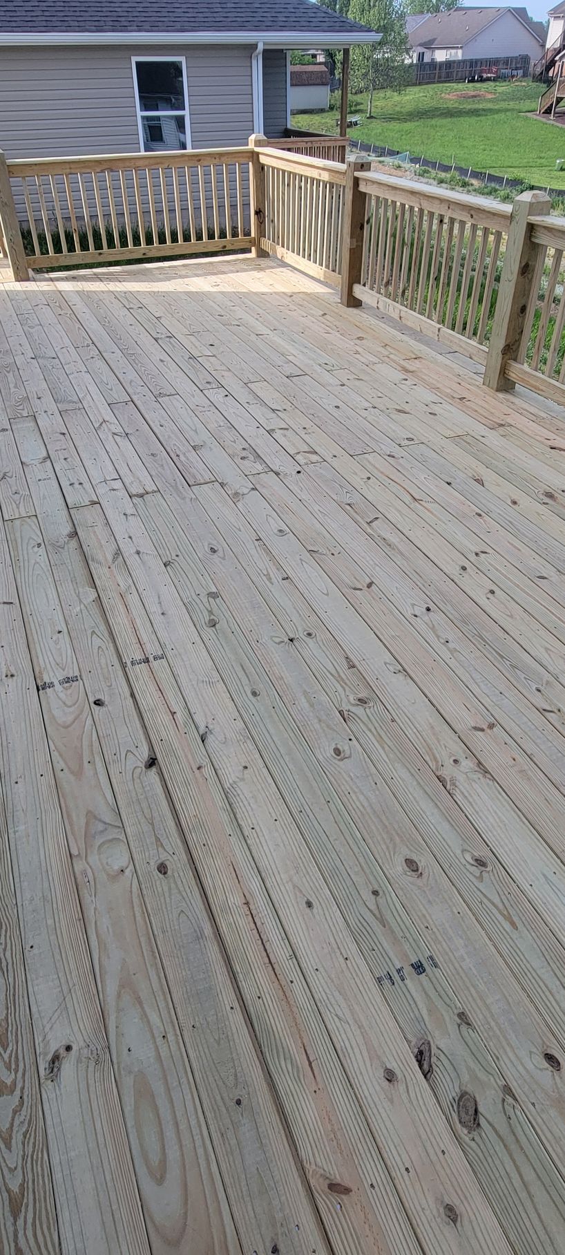 A wooden deck with a railing and a house in the background.