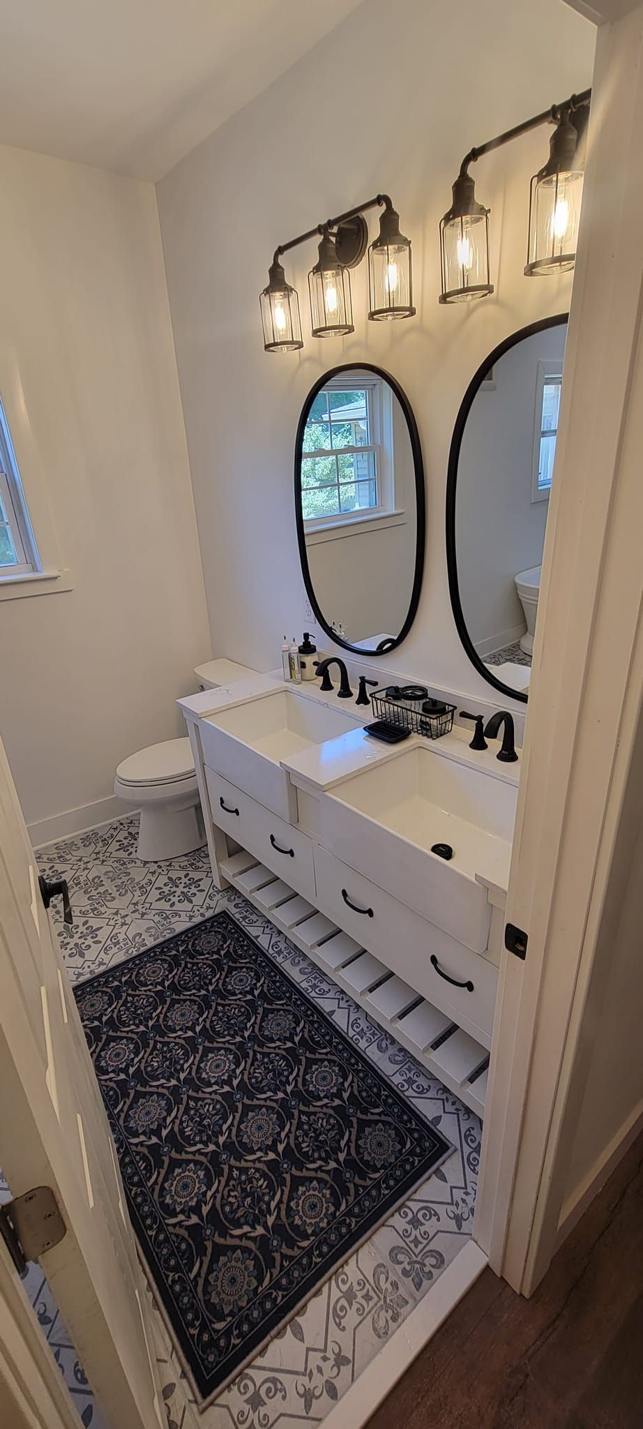 A bathroom with two sinks , two mirrors , a toilet and a rug.