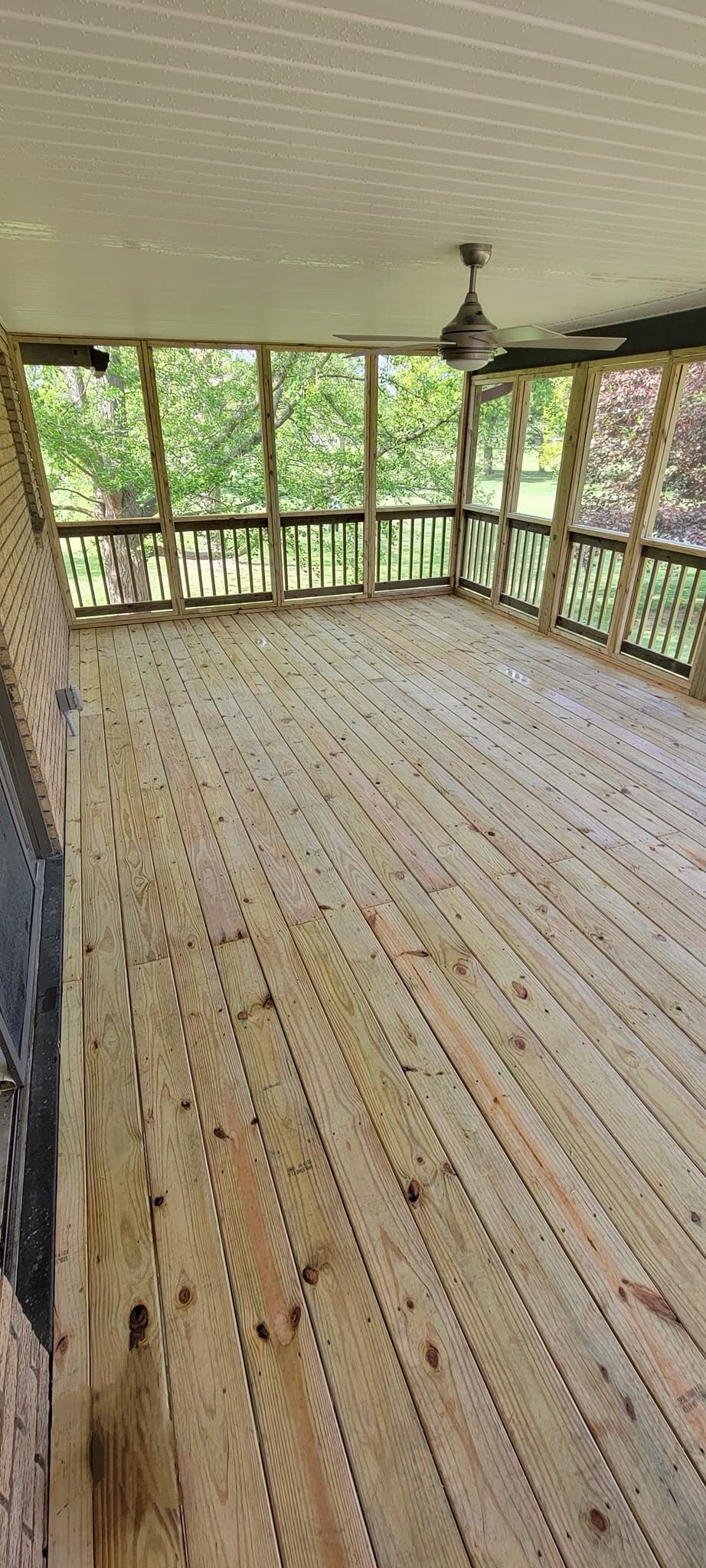 A screened in porch with a wooden floor and ceiling fan.
