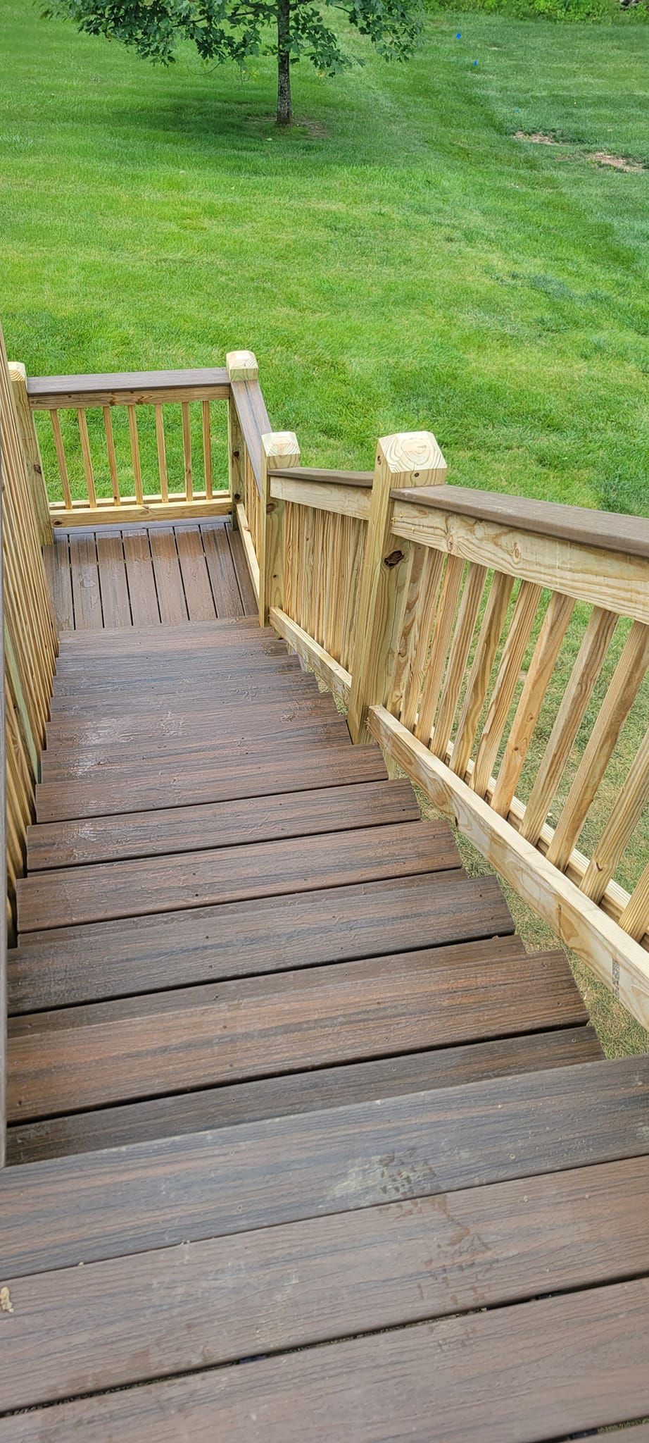 A wooden deck with stairs leading up to a grassy field.