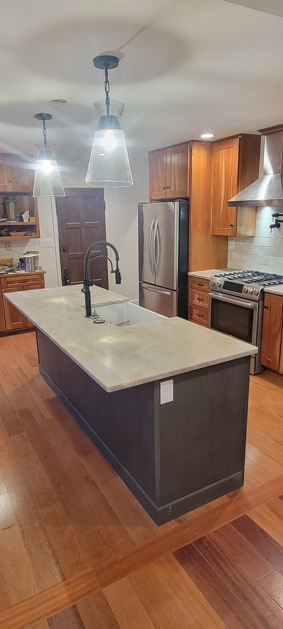 A kitchen with a large island , sink , stove , refrigerator and stainless steel appliances.